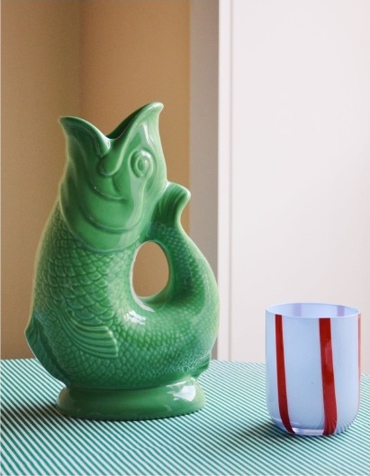 Green ceramic fish jug beside a striped glass on a green tablecloth