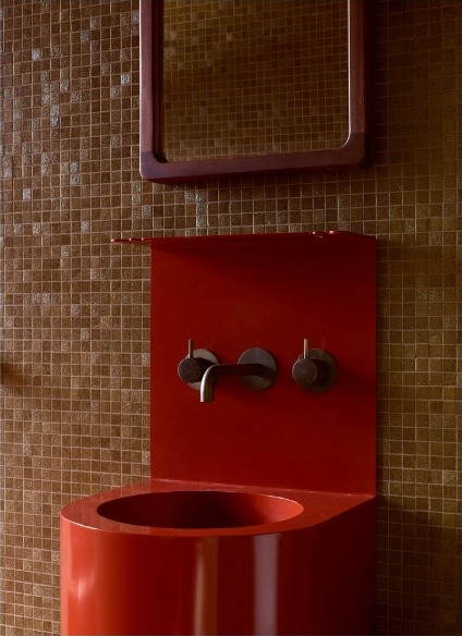 Bold red pedestal sink and mirror against brown mosaic tile